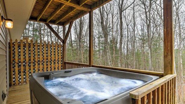 Un jacuzzi en una terraza de madera con vistas a un bosque.