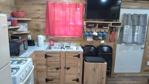 Una cocina compacta con armarios de madera, estufa a gas, microondas, lavabo y televisor.