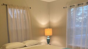 A bedroom with a bed, a nightstand, a lamp, and sheer curtains. - Walking distance to Baum Stadium & Razorback Greenway access across the street! (Fayetteville)