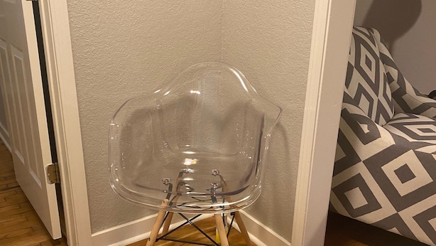 A clear plastic chair with wooden legs against a wall, wooden flooring, and a patterned sofa. - Walking distance to Baum Stadium & Razorback Greenway access across the street! (Fayetteville)