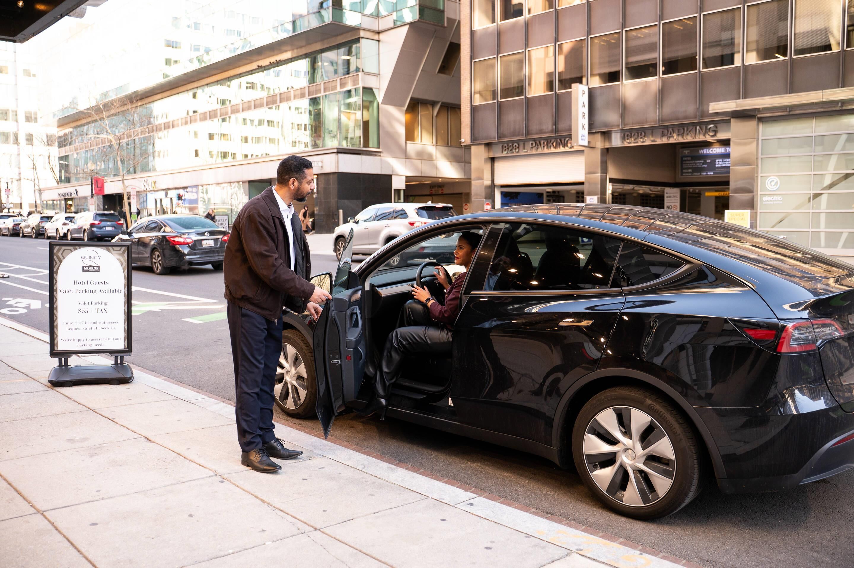 A black car parked on a city street with a valet sign nearby.