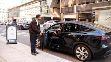 Un cotxe negre estacionat al carrer d'una ciutat, amb un senyal de pàrquing amb personal.
