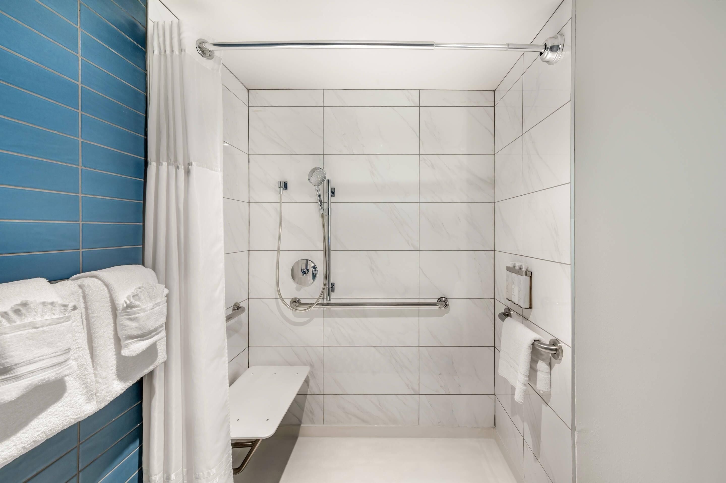 A modern bathroom with a shower, white tiles, a bench, and a towel rack.