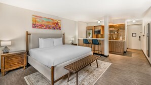 A bedroom with a bed, bedside tables, a bench, a desk, and a kitchenette. - The Quincy, an Ascend Collection Hotel (Washington)