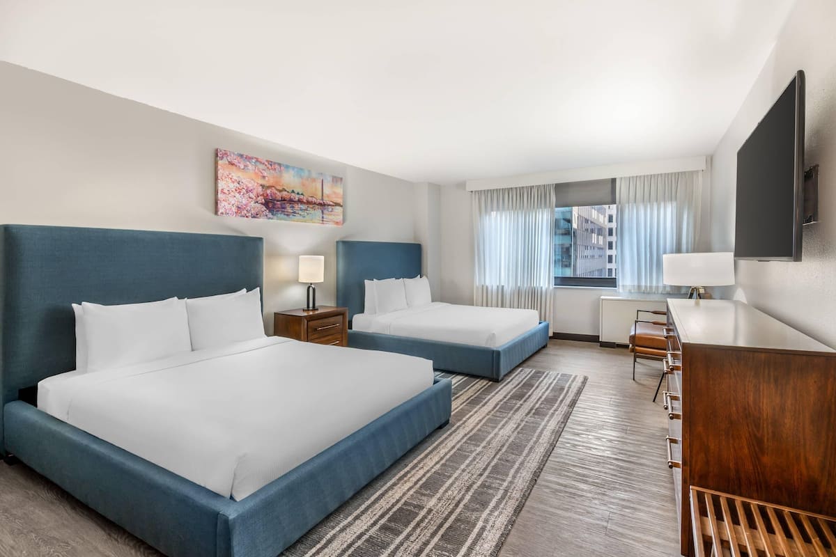 Une chambre d’hôtel avec deux lits, un bureau, une télévision et une fenêtre avec des rideaux.