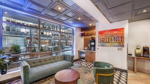 A lobby with a sofa, chairs, a coffee machine, and a large window with a view of the street. - The Quincy, an Ascend Collection Hotel (Washington)