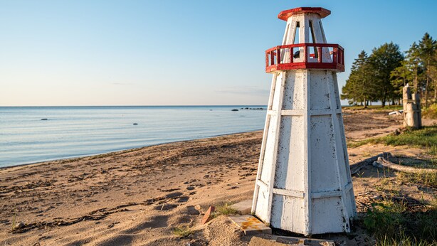 Ein Leuchtturm an einem sandigen Strand unter blauem Himmel.