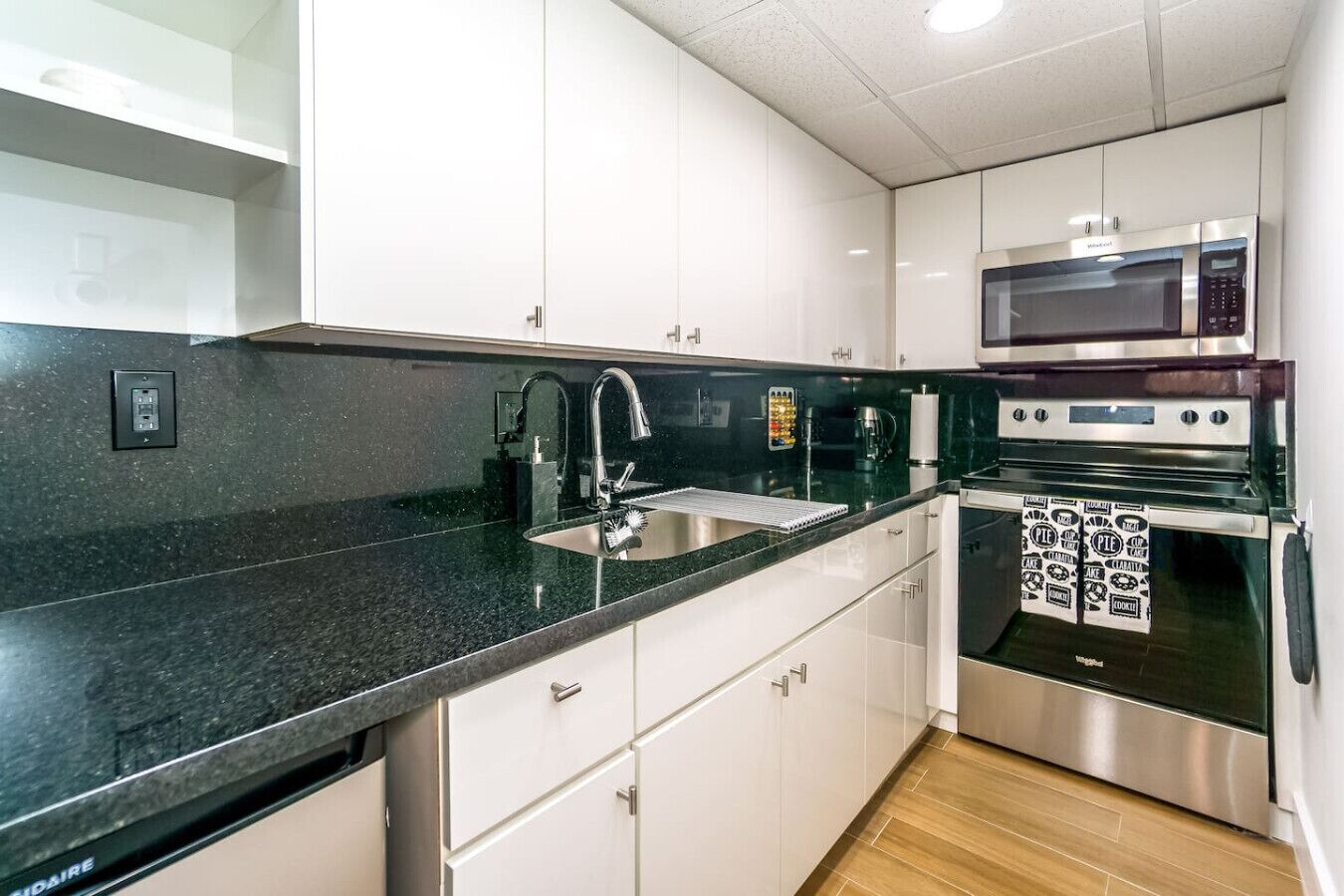 Een moderne keuken met witte kastjes, een zwart granieten aanrecht, roestvrijstalen apparatuur en een inbouwoven.