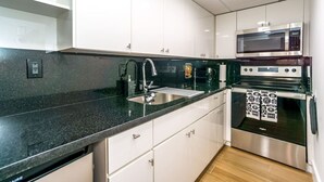 A modern kitchen with white cabinets, a black granite countertop, stainless steel appliances, and a built-in oven.