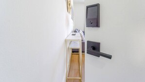 A hallway with a white door, a small table with a chair, and a wall-mounted device.