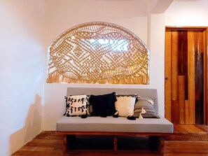 Ein Zimmer mit grauem Sofa, einer dekorativen Wandweberei und einer Holztür.