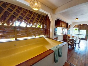 Ein Zimmer mit einer grossen Badewanne, Holzbalkendecke und einer Küchenzeile.