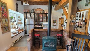 A cozy kitchen with a brick stove, wooden bar stools, and a black rocking chair. - Stone Road Log House (Westport)