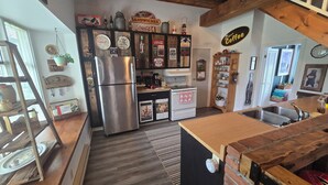 A kitchen with a stainless steel refrigerator, a stove, and a sink. There are various decorative items and signs on the walls. - Stone Road Log House (Westport)