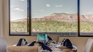Un coin repas avec une table dressée pour deux personnes, offrant une vue panoramique sur les formations rocheuses rouges et la végétation environnante.