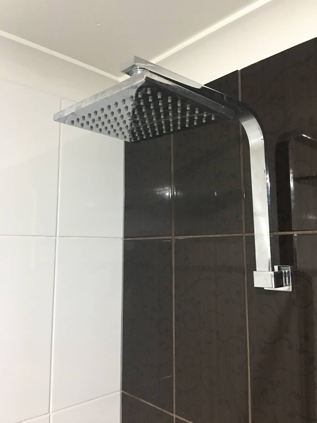 Una ducha moderna con un cabezal cuadrado y un grifo curvo.