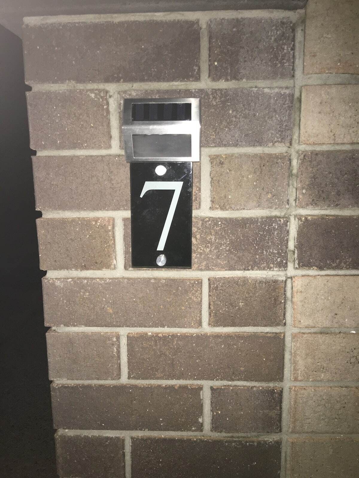 A black house number sign with the number 7 on a brick wall.