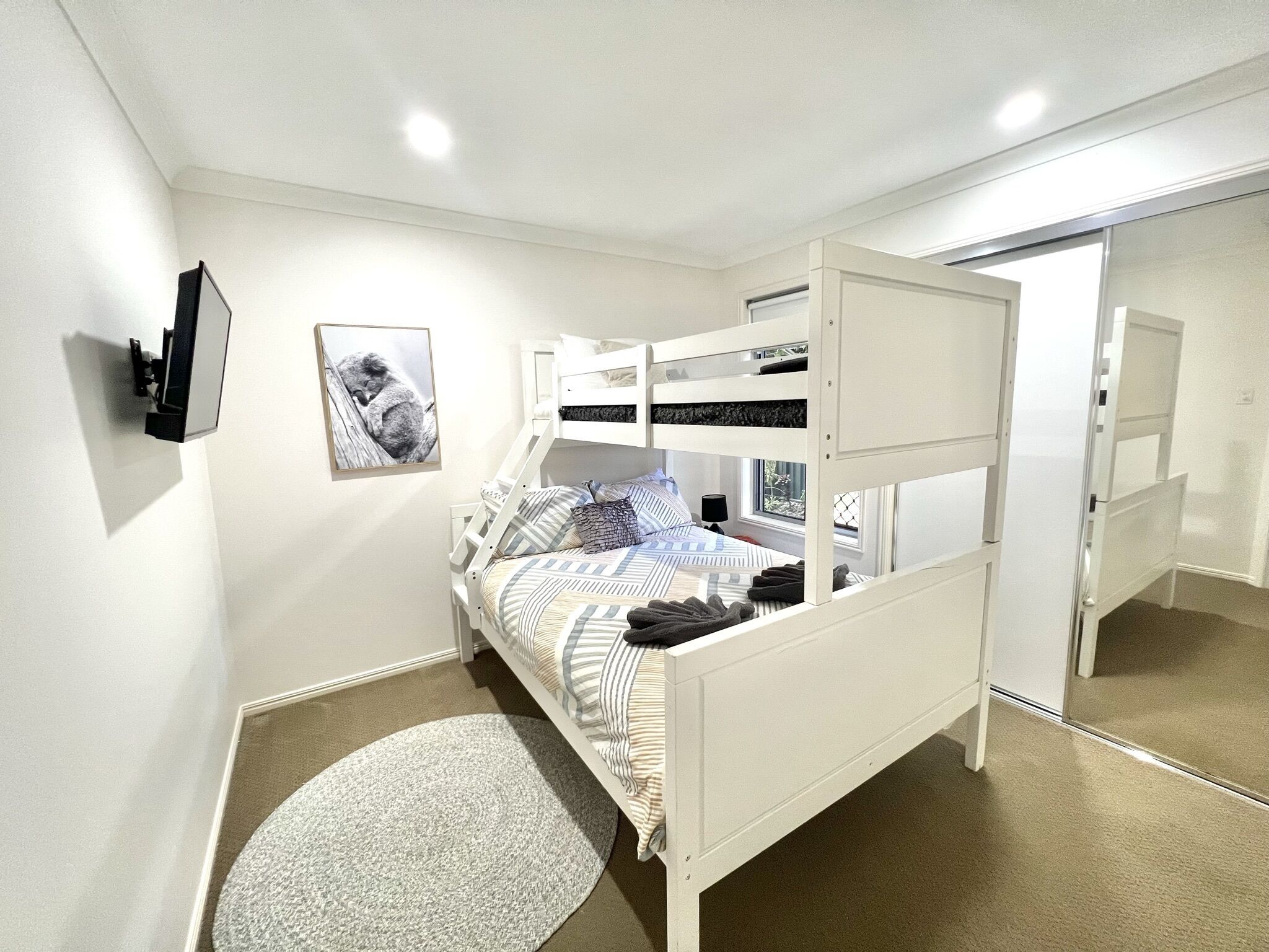 Una cama litera con una cama inferior, una mesita de noche, una lámpara, un cuadro en la pared y una alfombra redonda.