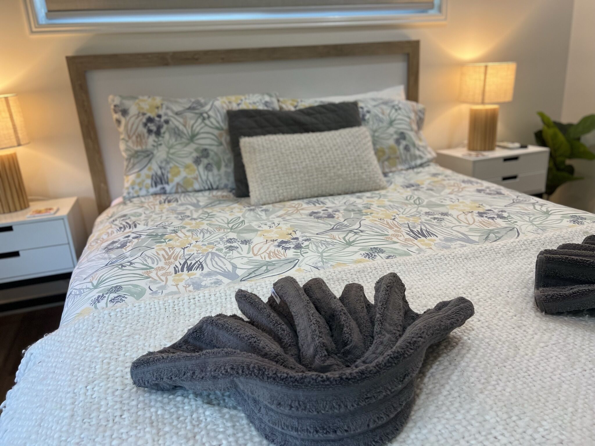 Un lit bien fait, avec une literie à motifs floraux, une tête de lit et deux lampes de chevet.