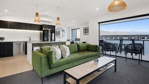 A modern living room with a green sofa, a coffee table, and a balcony with outdoor seating. - Hot Tub Retreat, 4 Ensuites, Mountain Views (Queenstown)