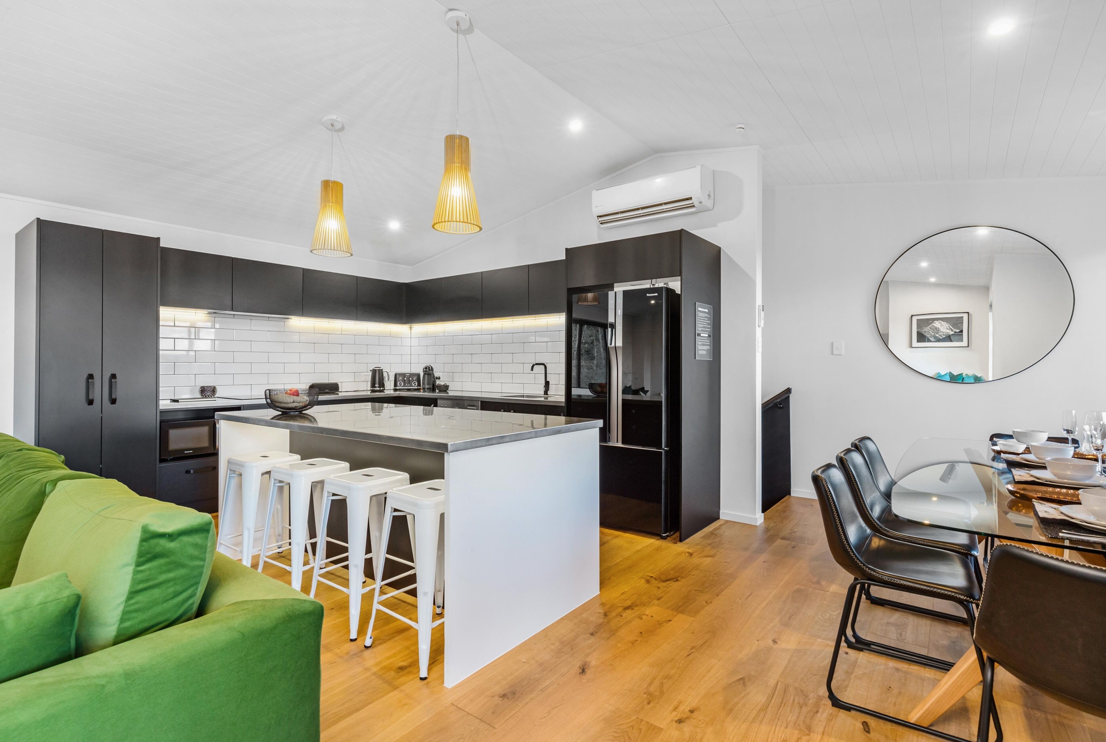 Una cocina moderna con una isla central, taburetes de bar, una mesa de comedor con sillas e iluminación colgante.