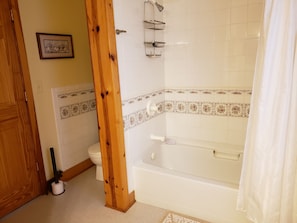 Et badeværelse med badekar, toilet og bruser.