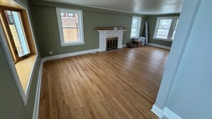 A spacious room with hardwood flooring, a fireplace, and large windows.