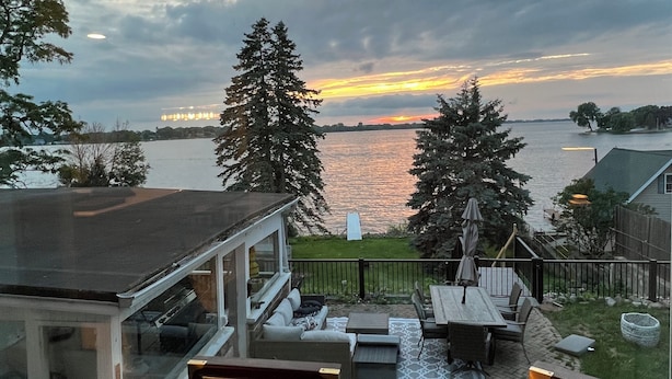A view from a window overlooking a backyard with a patio, a dining table, and a deck.