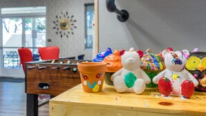 Een kamer met een tafelvoetbaltafel, een klok aan de muur en kleurrijke keramische dierenbeeldjes op een tafel.