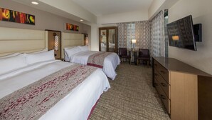 Een hotelkamer met twee bedden, een bureau, een stoel, een televisie en kunstwerken aan de muur.