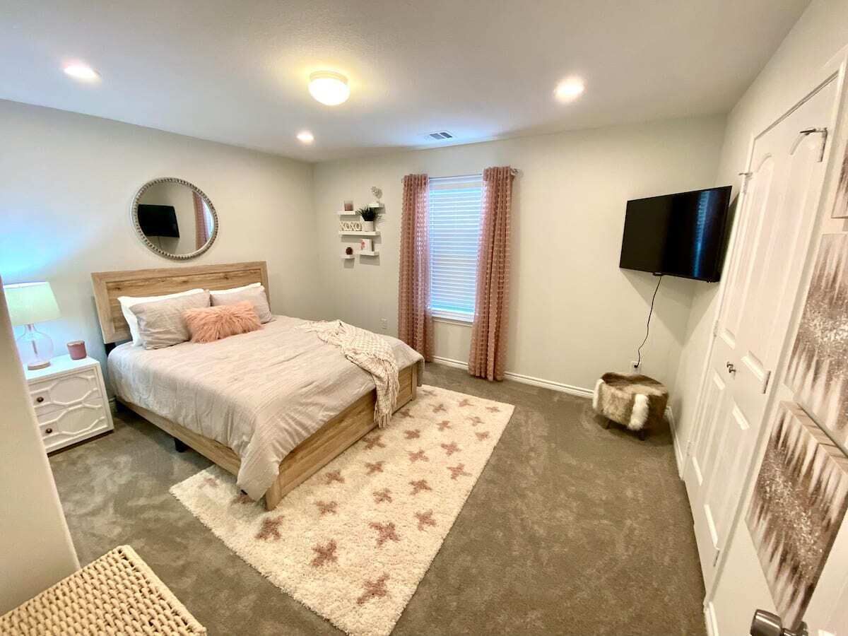 Une chambre à coucher avec un lit, des tables de chevet, une télévision, une fenêtre avec des rideaux et un tapis.