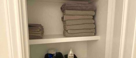 Un armario con repisas que guardan ropa doblada, toallas y cajas de almacenamiento.