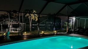 En swimmingpool med en klar blå vandoverflade, omgivet af et overdækket område med en metal konstruktion.