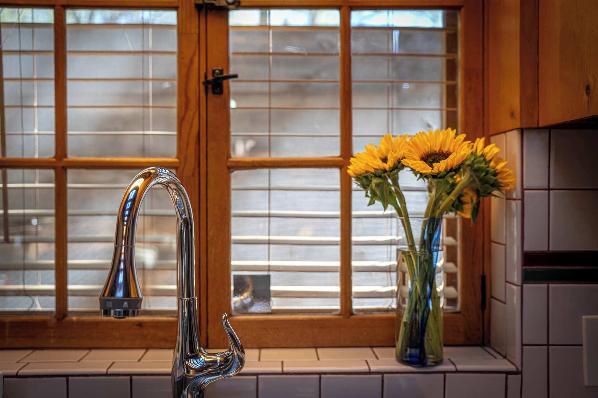 A kitchen with a modern faucet, a window with blinds, and a vase with sunflowers.
