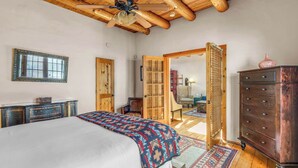 Une chambre à coucher avec un lit, des poutres apparentes en bois au plafond, un ventilateur de plafond, une commode et une armoire.