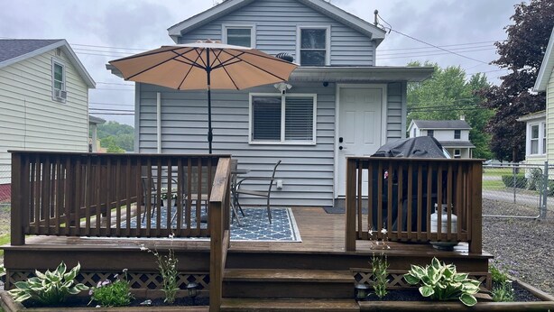 Ein zweistöckiges Haus mit einer Holzterrasse, einem überdachten Patio und einem kleinen Garten mit verschiedenen Pflanzen.