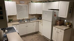 Eine kleine Küche mit weißen Schränken, einem Kühlschrank, einer Spüle und einer Arbeitsplatte.