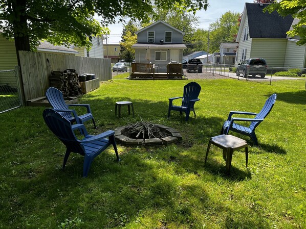 A backyard with a fire pit, four Adirondack chairs, and a wooden deck. - Updated & Clean Dog Friendly Cottage - Walk to Chautauqua Lake. Beautiful views! (Mayville)