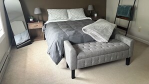 Ein Schlafzimmer mit Bett, Nachttischen, einem Spiegel, einer Bank und einem Regal.