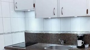 Eine kleine Küche mit weißen Schränken, einer Arbeitsplatte aus Granit, einem Edelstahlspülbecken und einer Kaffeemaschine.