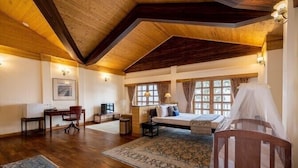 Una habitación amplia con techo de madera, una cama grande, un escritorio con silla y una ventana con cortinas.