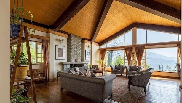 Amplia sala de estar con techo alto, vigas de madera, chimenea y ventanas grandes que ofrecen vistas al exterior.
