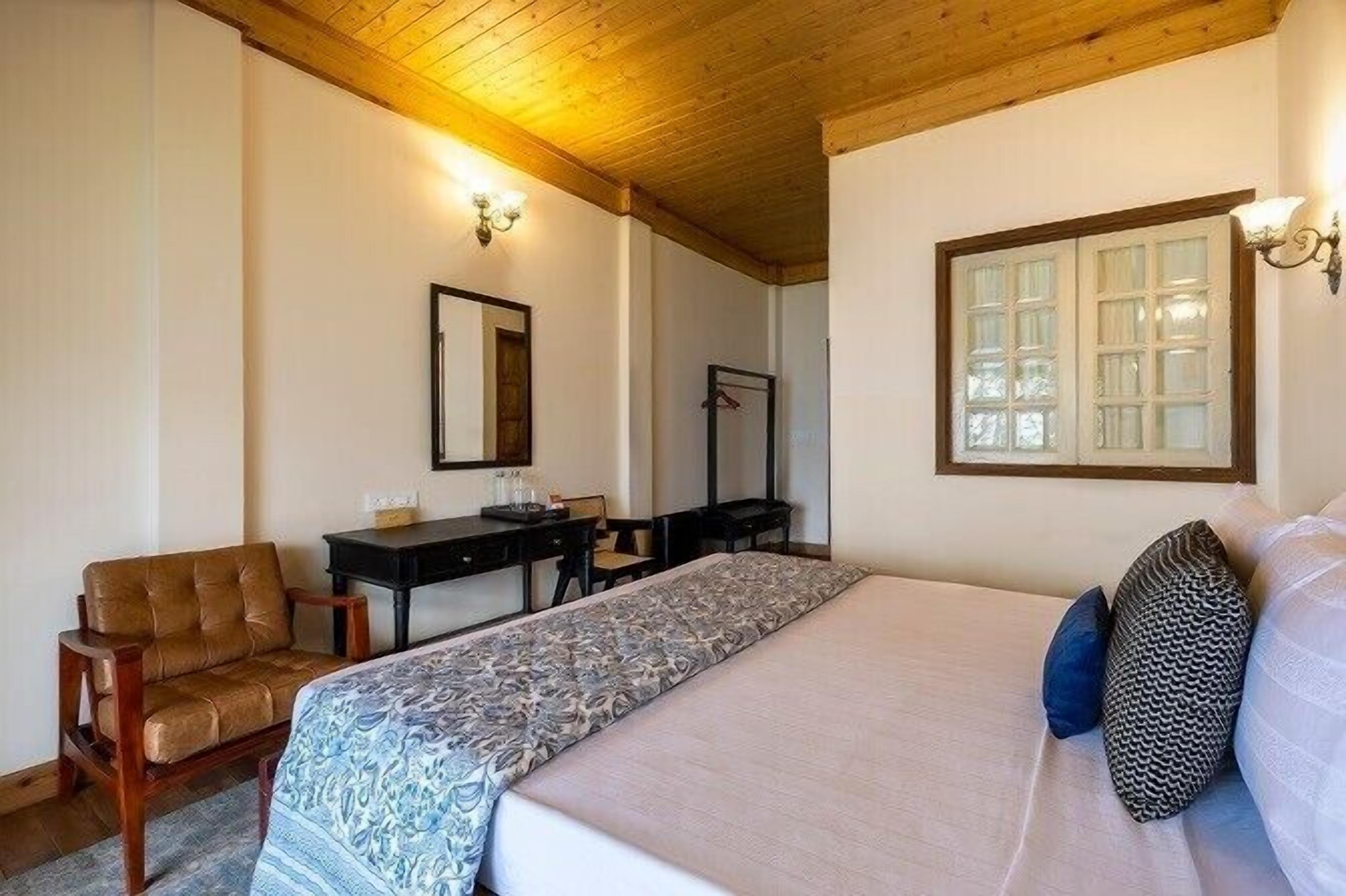 A hotel room with a bed, a desk, a chair, and a mirror.