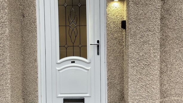Eine weiße Tür mit Glasfenster und kleinem Fenster, eine Nummernschild mit der Aufschrift "628 Crow Road" und einer Wandleuchte.