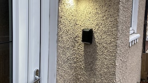 Eine strukturierte Wand mit einer Leuchte und einem kleinen, schwarzen Objekt, möglicherweise einem Briefkasten.