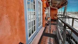 Un balcon avec une balustrade en métal, une fenêtre avec un cadre blanc et une petite étagère sur laquelle sont posés divers objets.
