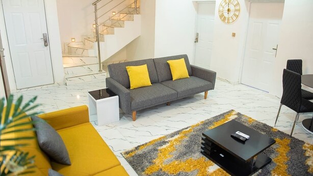 En moderne stue med en grå sofa, gule puder, et sort sofabord og en trappe, der fører op til en etage.