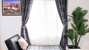 Ein modernes Wohnzimmer mit einem schwarzen Sofa, einer großen Topfpflanze und einem gerahmten Bild an der Wand.
