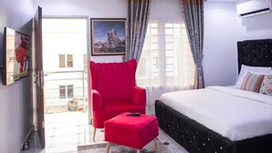 Ein Hotelzimmer mit einem Bett, einem roten Sessel, einem kleinen Tisch, einem Fenster mit Vorhängen und einem Gemälde an der Wand.