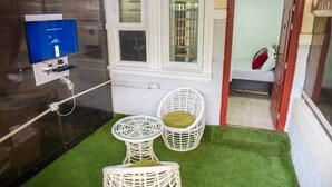 Een kleine kamer met een televisie, twee rieten stoelen, een raam en kunstgras.